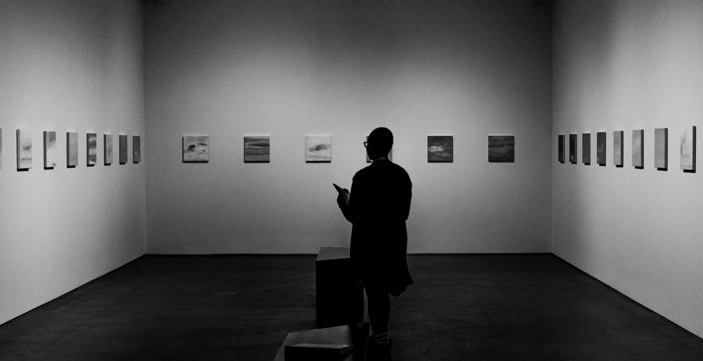 Silhouette of a person in an empty gallery lined with small framed works