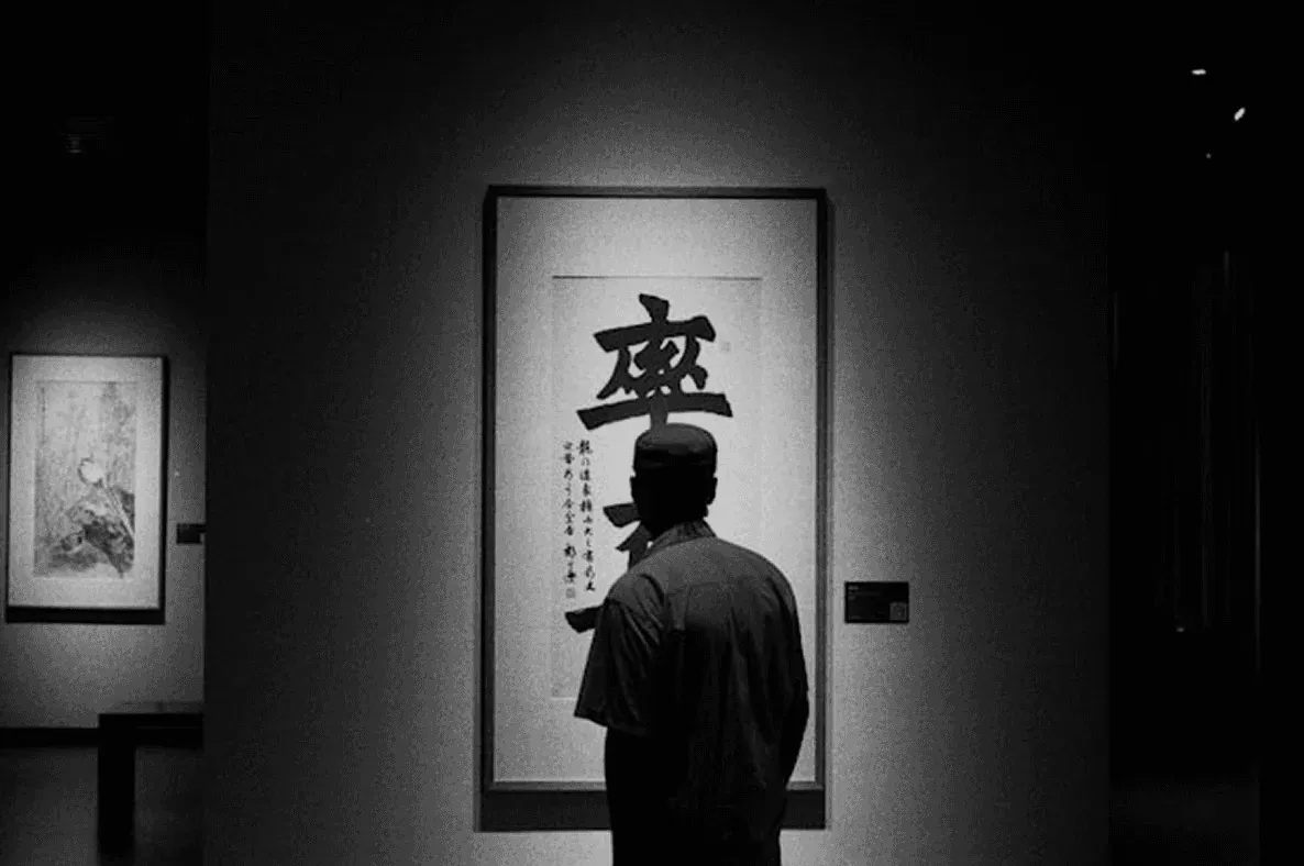 Visitor standing before a large calligraphy scroll in a dim gallery